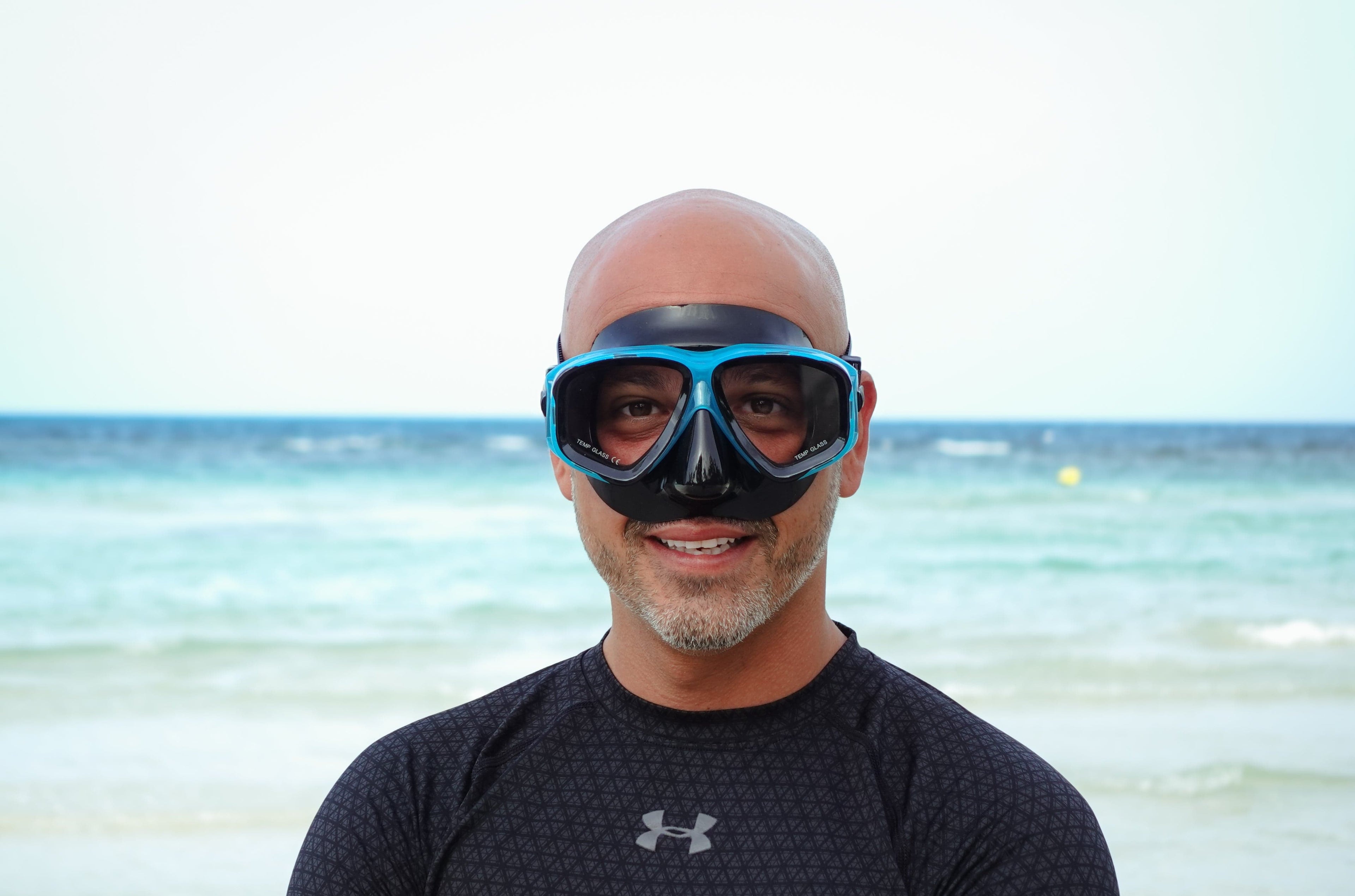 Man wearing a prescription snorkeling mask with a beach and ocean in the background