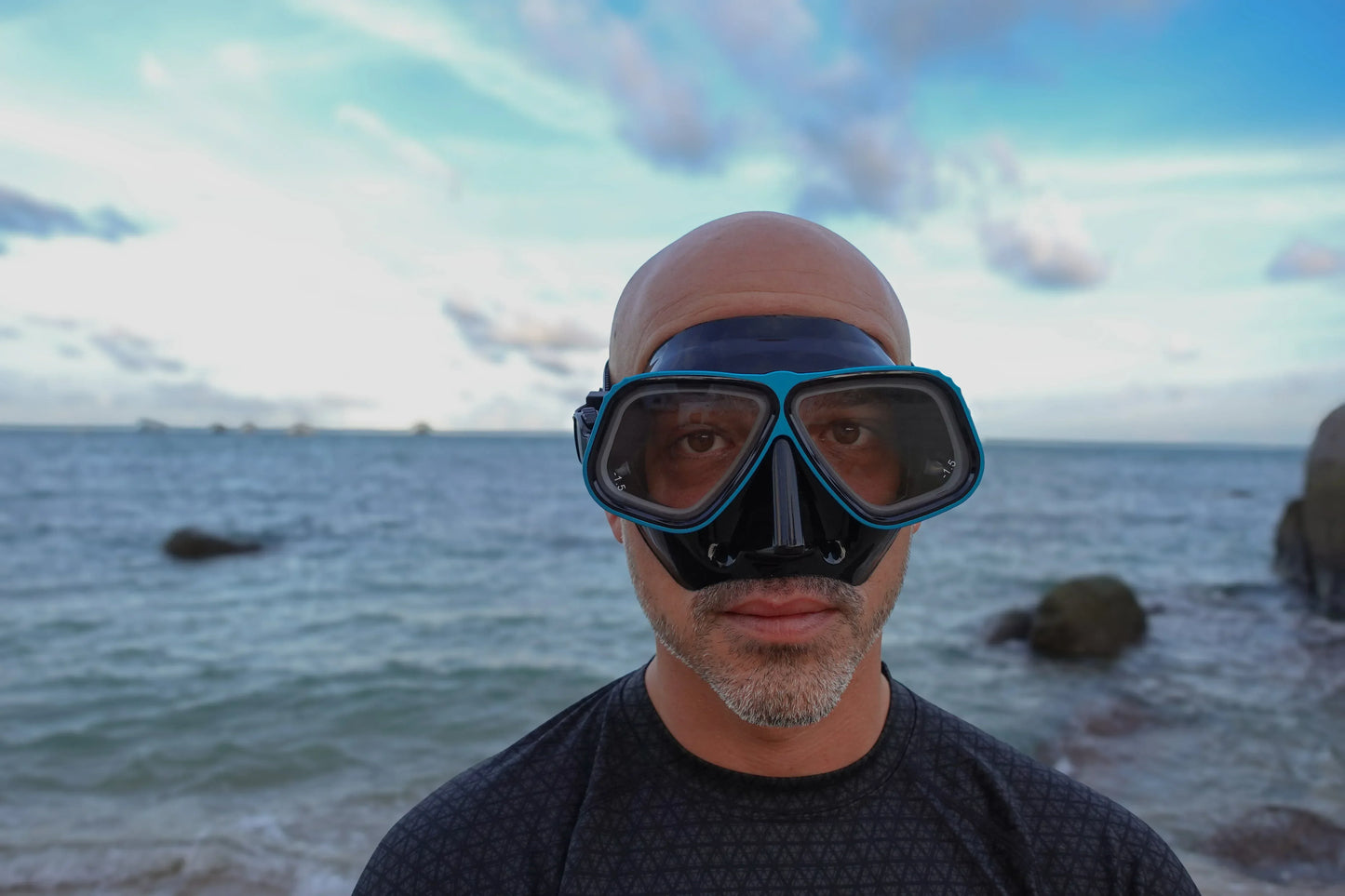 Man wearing Prescription scuba dive mask with Aluminium Blue frame and Black seal. The Rx Lumix mask. Standing in front of the ocean.