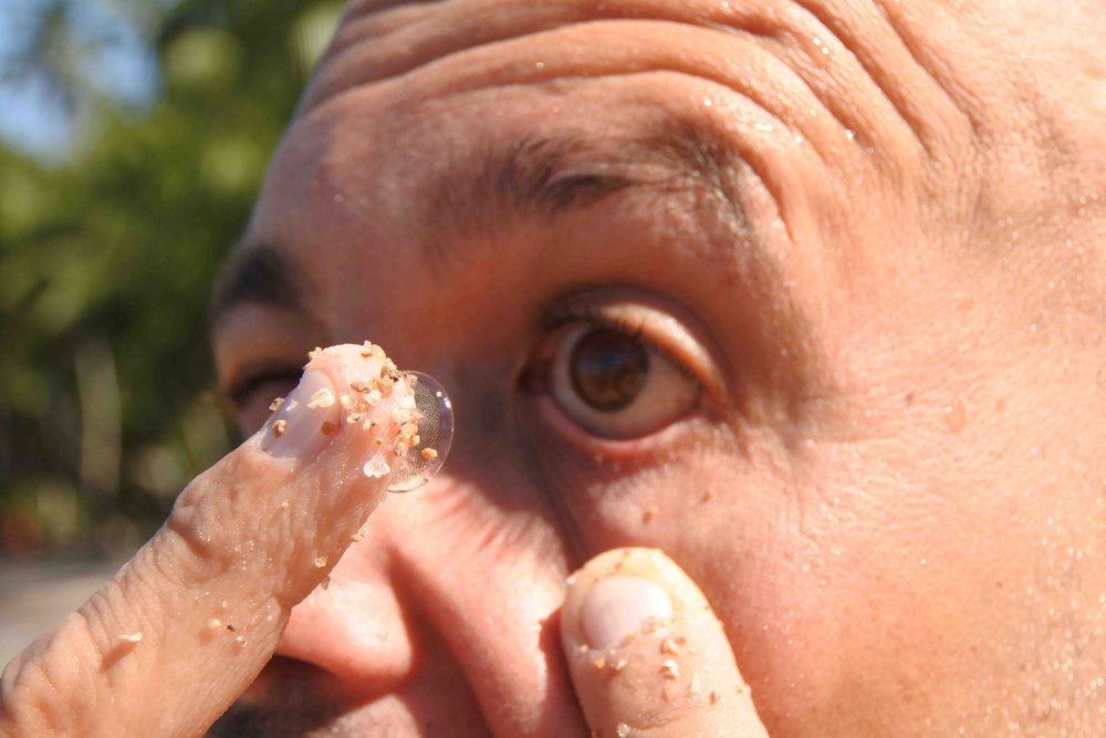finger with sand holding a contact lens about to be put onto a mans eye