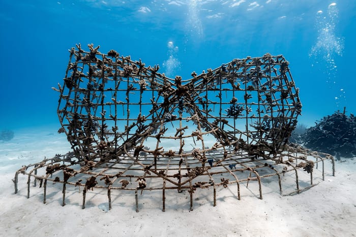 Metallic underwater coral reef sculpture with staghorn branching corals on a sandy ocean floor