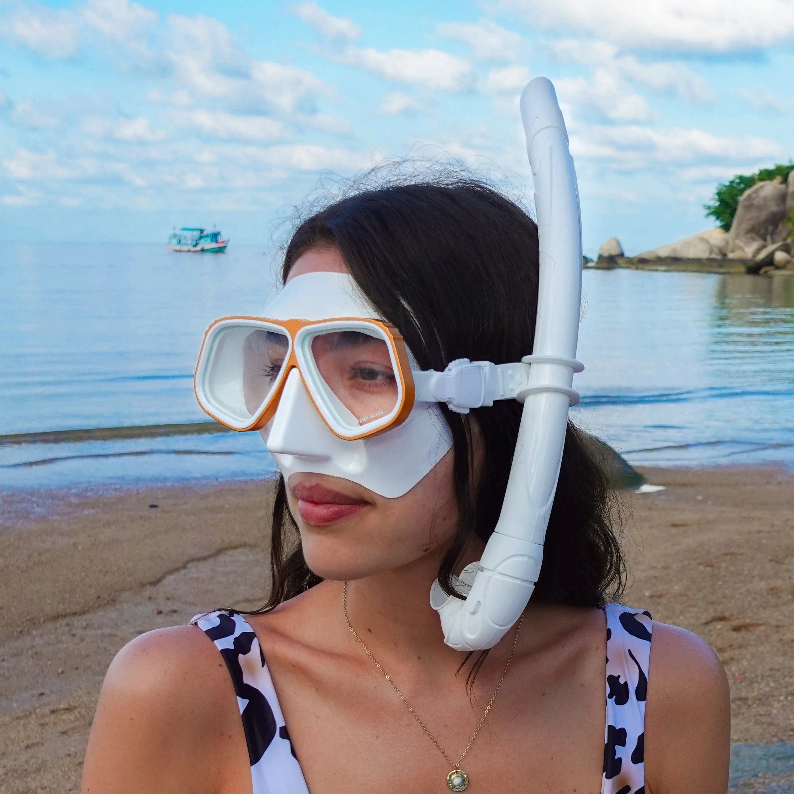 Woman wearing an Rx snorkel mask on a beach with a clear sky and water in the background